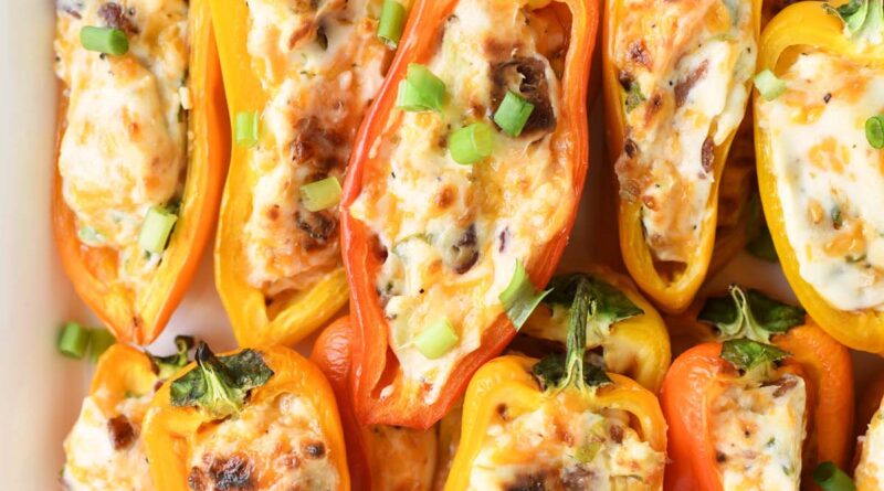 Colorful mini bell peppers stuffed with a creamy mixture of mashed avocado and crumbled bacon, garnished with fresh cilantro and optional shredded cheese, arranged on a white serving platter.